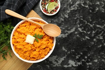 Delicious mashed sweet potatoes with butter, spices and spoon on dark table, top view. Space for text