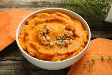 Delicious mashed sweet potatoes in bowl, walnuts and cut vegetable on wooden table, closeup