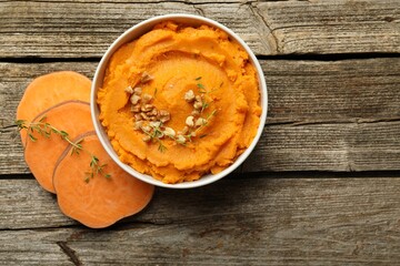 Delicious mashed sweet potatoes in bowl, walnuts and cut vegetable on wooden table, top view. Space for text