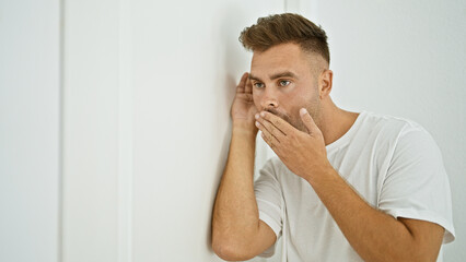A shocked hispanic man spying through a white door in a home setting.