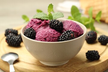 Delicious blackberry sorbet with fresh berries in bowl and spoon on table, closeup