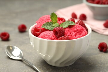 Delicious raspberry sorbet with fresh berries in bowl and spoon on gray textured table, closeup
