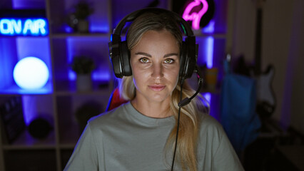 A confident young woman with headphones in a neon-lit gaming room at night.