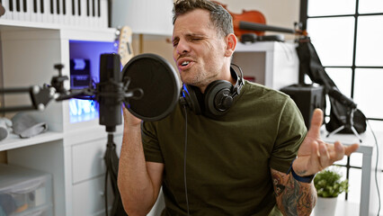 Hispanic man singing passionately in a music studio with a microphone and headphones
