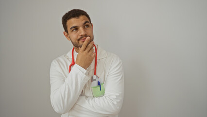 Young hispanic man isolated over white background with a thoughtful expression wearing a white lab coat and red stethoscope around his neck