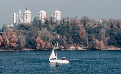 yacht with a white sail on the background of the coast and the city