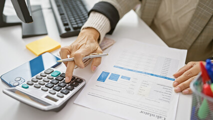 Mature hispanic woman working with calculator and financial documents at her office desk