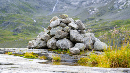 A carefully stacked cairn stands on a rocky terrain with lush greenery and a waterfall background.