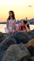 Two teenage girls friends, one slightly overweight and the other with dark skin, chatting and having a great time together by the seaside on a sunny summer day