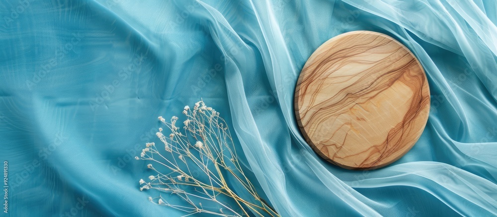 Poster Top view of a wooden disc on blue fabric with white tendrils providing ample copy space image