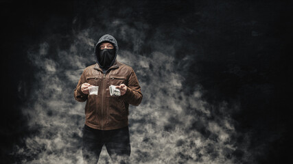 Drug dealer, dangerous hooded criminal man in black mask and brown leather jacket holding...