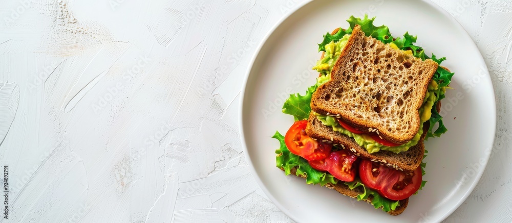 Poster a sandwich with guacamole and heirloom tomato on wheat bread displayed on a white plate against a wh