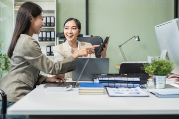 Business documents on office table with tablet and laptop computer and chart and two colleagues discussing data in office.