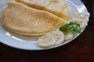 Banana crepes with Honey on a white plate. with brown background.
