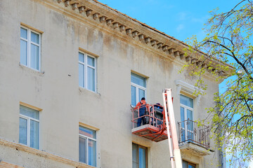 Worker at height in lifting bucket installing new window sill, historic building renovation. Man...