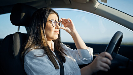 Young beautiful hispanic woman driving a car with sunlight on face on the road