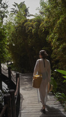 Fototapeta premium A young woman strolls through a lush balinese resort path, embodying tranquility and leisure in a tropical setting.