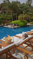 A young woman relaxes by a resort pool in bali, showcasing leisure, travel, and luxury in a tropical setting.