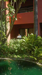 A young woman enjoys tranquility on a bali resort terrace, surrounded by lush greenery and a serene pool.