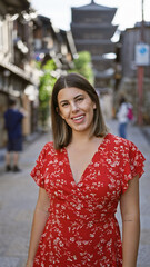 Naklejka premium Cheerful, beautiful hispanic woman smiling confidently on kyoto's old gion street, radiating positive emotions and genuine joy while casually posing in front of traditional wooden pagoda.