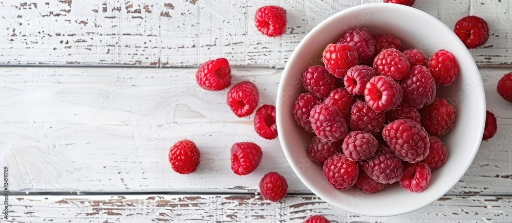 Poster Fresh red raspberries displayed in a white bowl on a light rustic wood backdrop in a top view image with available copy space and selective focus for a vegetarian context