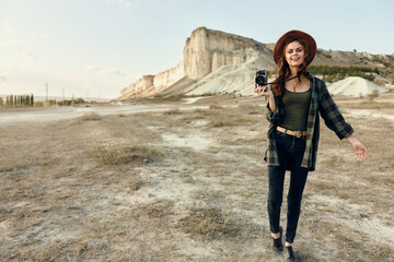 female photographer in plaid shirt and hat capturing nature with camera in open field