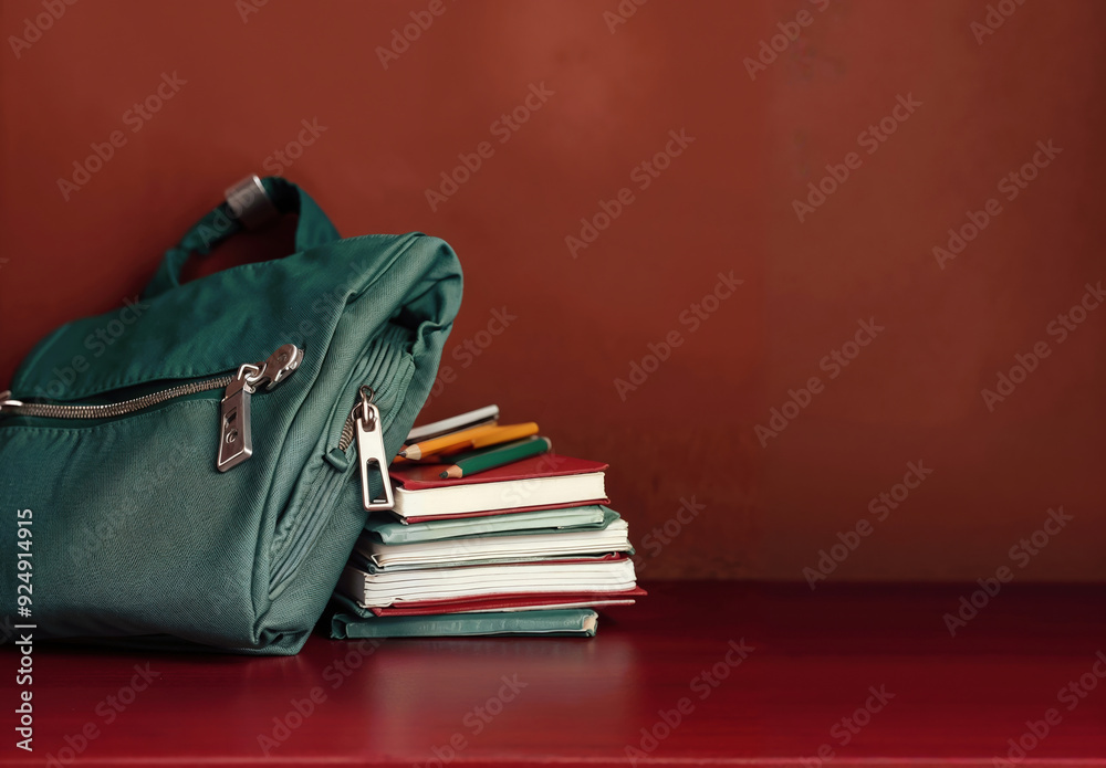 Aufkleber Green backpack on stack of books and pencils on red table and red wall background with copy space for back to school