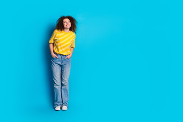 Fototapeta premium Full length photo of lovely young lady hands pockets pose look empty space dressed striped yellow garment isolated on blue color background