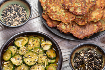 Zucchini and chickpea flour pancakes, sliced cucumbers pickled in soy sauce. In small bowls are: shiso leaves pickled in soy sauce, and black and white sesame seeds. Vegan snack or lunch.