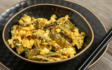 Homemade bitter melon stir-fry with eggs on a plate with chopsticks.