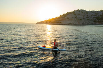 Man in orange vest navigating on the paddleboard in the sea at sunset.