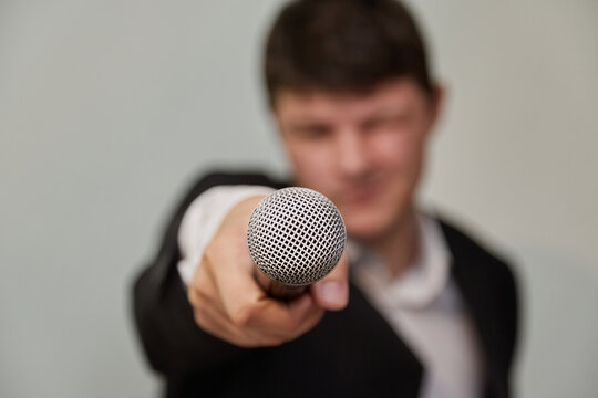 Blurred image of a young man pointing a microphone at the viewer. Journalistic interview, aggressive behavior of a journalist, public survey, journalist's work, journalistic investigation