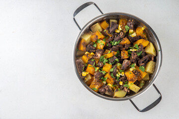 Warm pumpkin stew with potato and beef meat, comfort autumn dinner balanced food, with ingredients on kitchen table