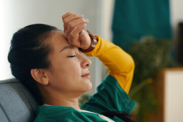Woman resting on couch with hand resting on forehead and eyes closed showing moment of peace and...