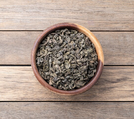 Dried green tea leaves on a bowl over wooden table