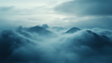 A breathtaking view of a mountain range peeking through a sea of clouds, bathed in soft, blue light.