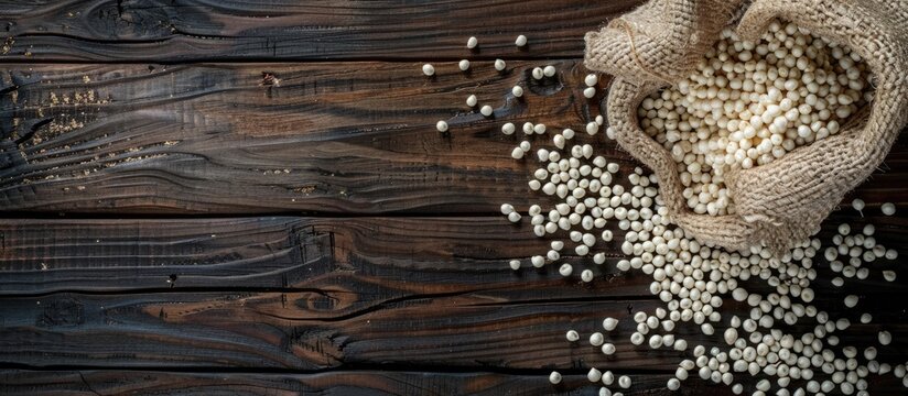 Top view of spilled organic whole pearl millet or Bajra seeds from a jute bag with Bajra Flour on dark wood isolated background with copy space image