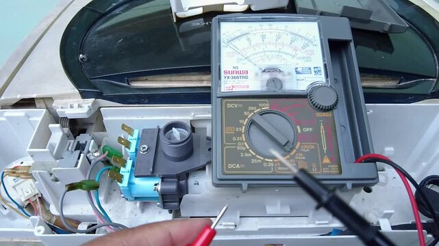 14,Aug,2024,lopburi Thailand,Hands of a technician using an ohmmeter to check a damaged water valve of a washing machine.
