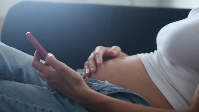 Pregnant woman at 14 weeks chatting and consulting her mobile phone, sharing news, and touching her belly. Gestational diabetes, pregnancy, first trimester, reproductive health