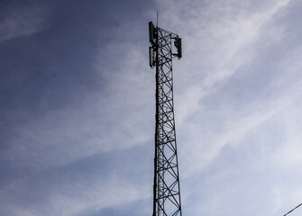 Selective focus of  telecommunications towers with a background of bright blue sky with clouds and trees during the day