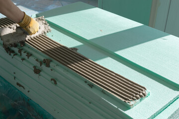 Construction worker applying adhesive mortar onto XPS (Extruded Polystyrene) board with bricklayer notched trowel.