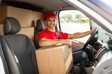 Obraz premium Express delivery. Happy courier guy sitting in van full loaded with parcels and boxes, looking and smiling at camera