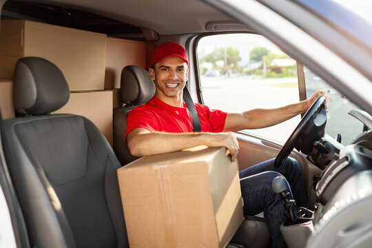 Express delivery. Happy courier guy sitting in van full loaded with parcels and boxes, looking and smiling at camera