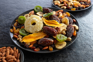 Dried tropical fruits, nuts, and raisins in black plate.