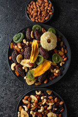 Dried tropical fruits, nuts, and raisins in black plate.