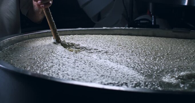 Super slow motion close up of artisan cheesemaker is mixing fresh bio eco milk during traditional cheese making process at cheese production creamery dairy factory at 1000 fps.