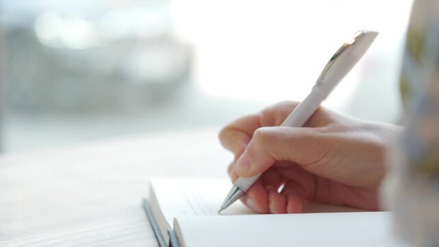 A closeup of a hand writing in a notebook with a pen, capturing a moment of creativity and productivity