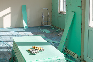 Indoor thermal insulation materials . XPS (Extruded Polystyrene) boards and work gloves in selective focus. Out of focus, Indoor thermal insulation materials mounted on the wall of a room.  