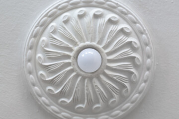 Energy-saving ceiling light bulb and ornamental round plasterboard cornice close-up.
