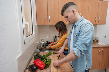 Young couple cooking together on a kitchen. Man and woman vegan cook vegetables for meal. Healthy lifestyle